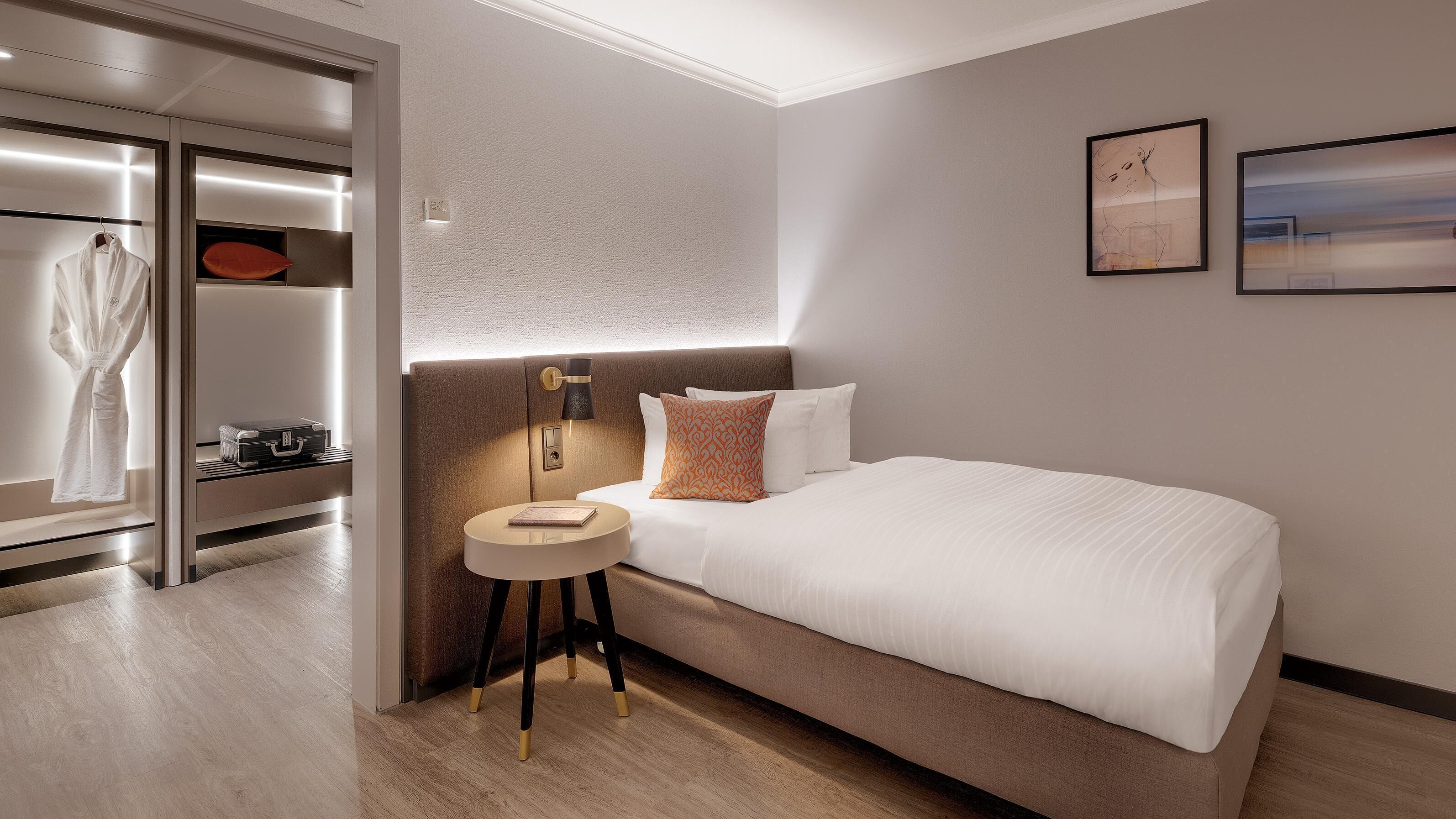 Una habitación de hotel moderna con una cama grande, una mesita de noche, una bata colgada y un armario con espejo.
