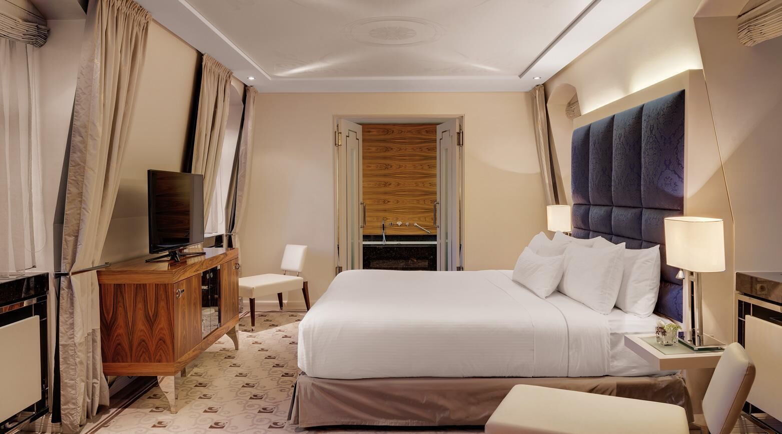 A hotel room with a large bed, a wooden dresser, a television, and a desk with a lamp.