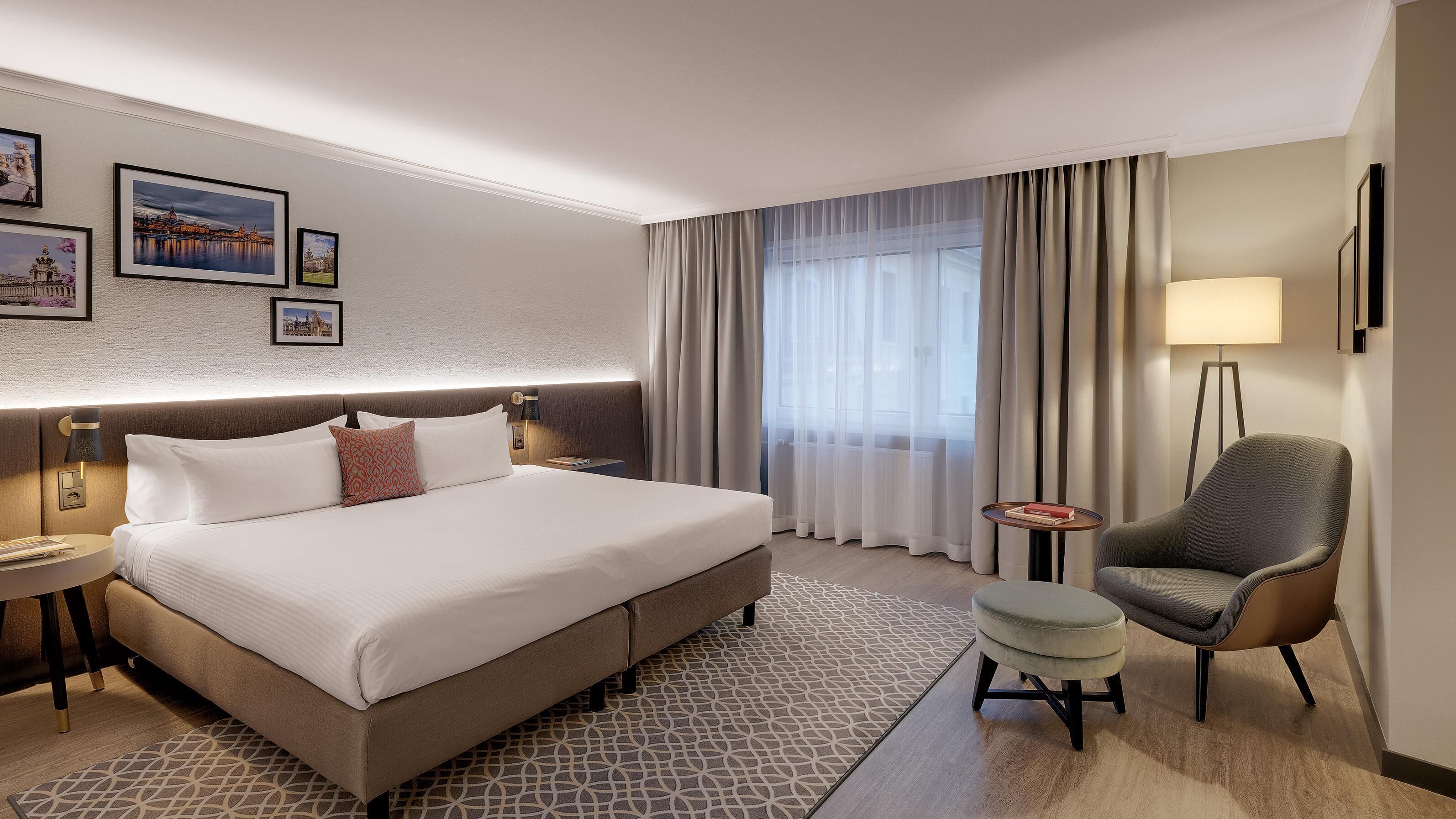 A hotel room with a large bed, a chair, a small table, and a nightstand.