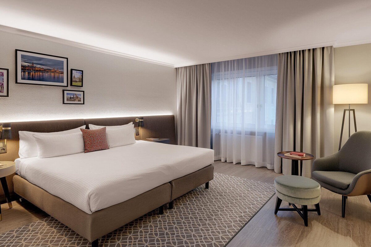 A hotel room with a large bed, a chair, a small table, and a nightstand.