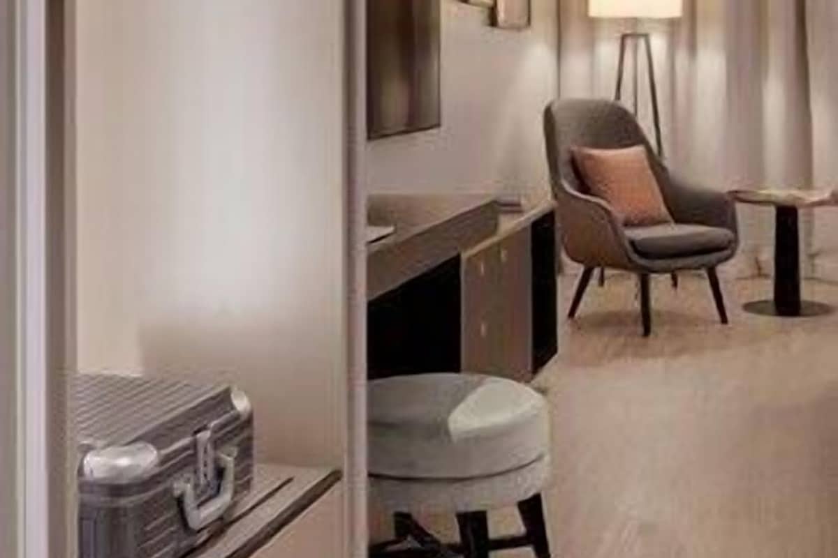 Habitación de hotel con cama, escritorio, silla, lámpara y maleta.