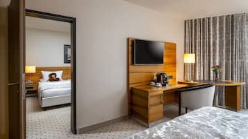 A hotel room with a bed, a desk with a flat-screen TV, a chair, a lamp, and a vase with flowers.