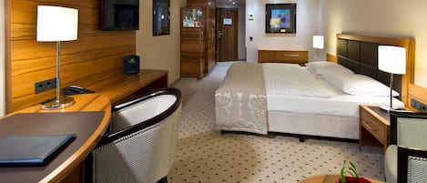 A hotel room with a bed, desk, chair, TV, wardrobe, and a small table with a vase of flowers.