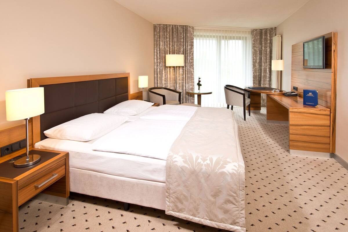 A hotel room with a large bed, two bedside tables, a desk, a chair, a lamp, and a television.