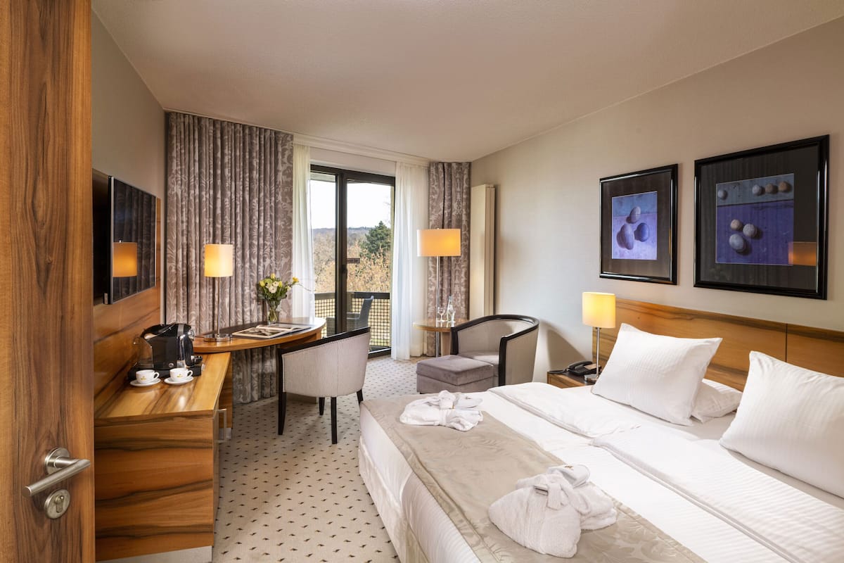 A hotel room with a bed, a desk, a chair, a small table with a coffee maker, and a view of the outdoors.