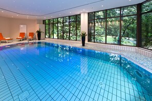An indoor swimming pool with clear blue water, surrounded by large windows offering a view of trees. - Maritim Hotel Bad Homburg (Bad Homburg v.d. Hoehe)