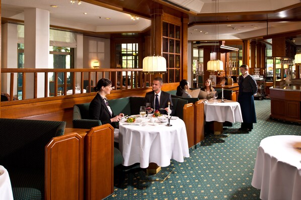 A formal dining area with wooden paneling, green patterned carpet, and white tablecloths. - Maritim Hotel Bad Homburg (Bad Homburg v.d. Hoehe)