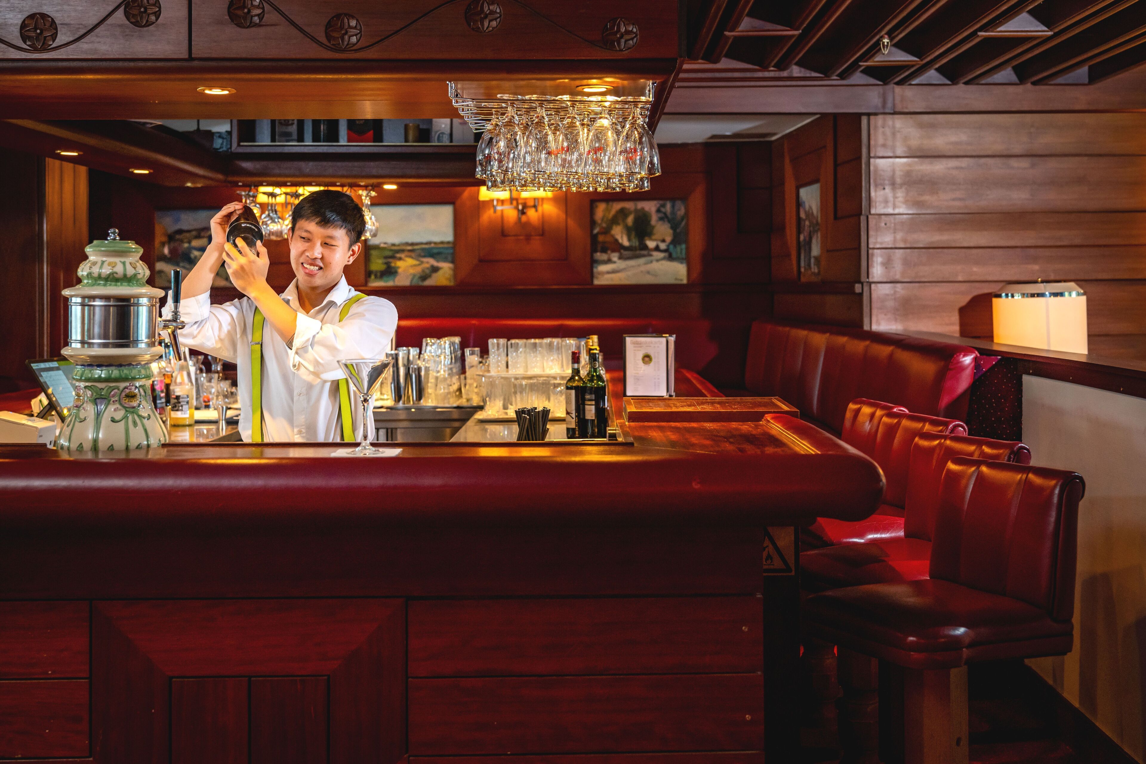 A bar area with a bartender, a wooden bar counter, and leather seating.