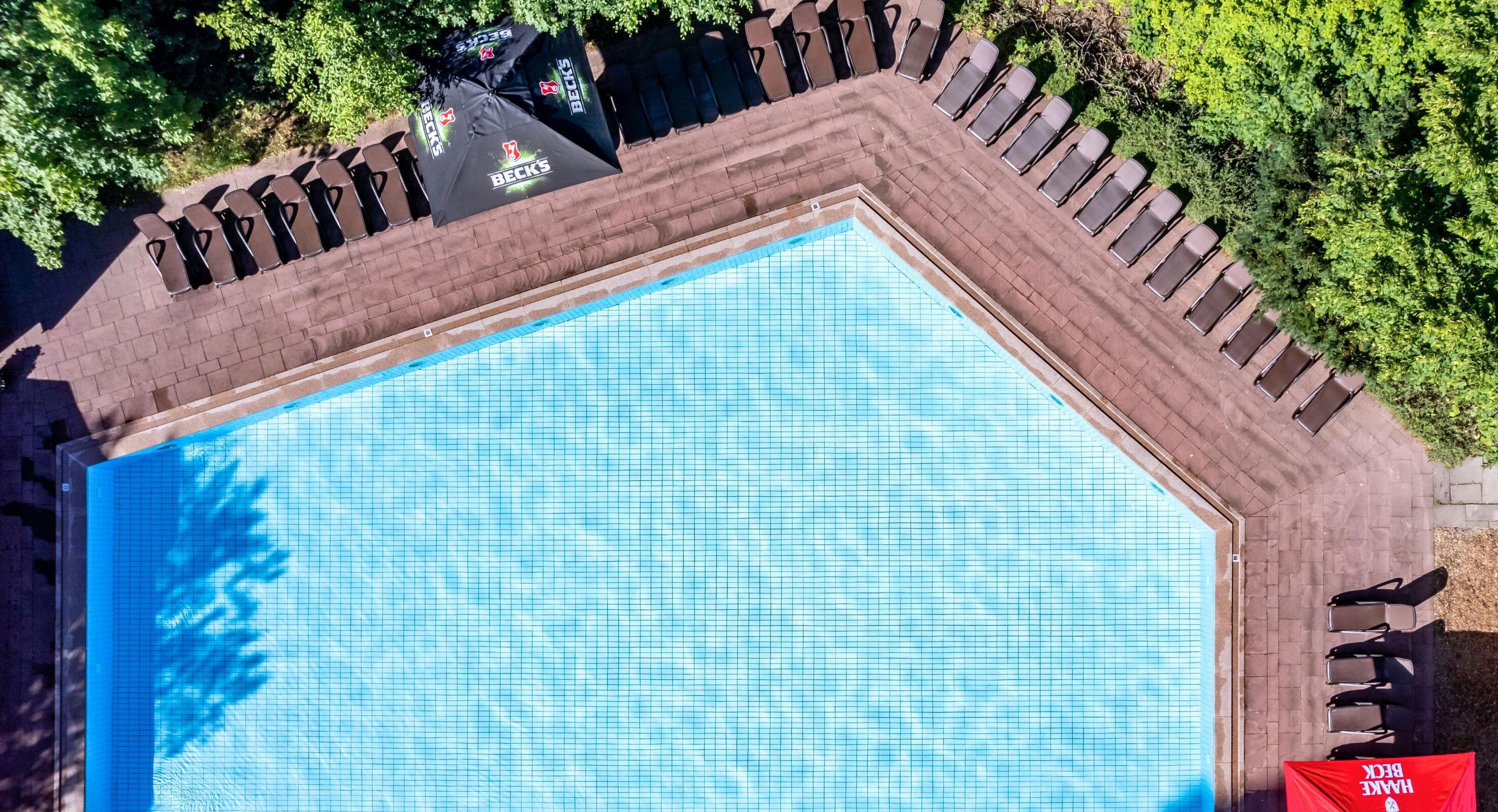 Vista aérea de una piscina con sillones de descanso y sombrillas.