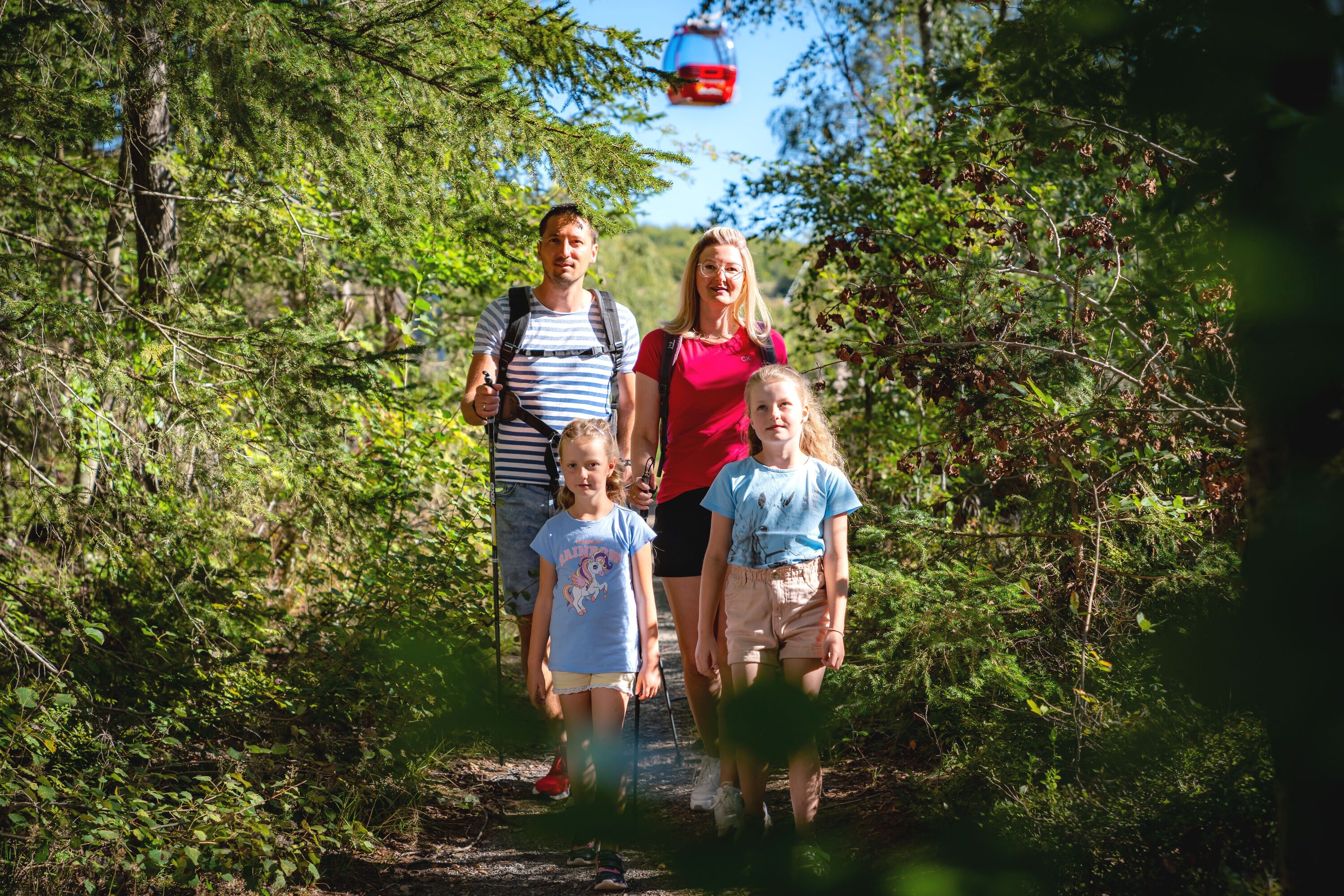 Una familia caminando por un sendero en un bosque, con abundante vegetación a ambos lados.