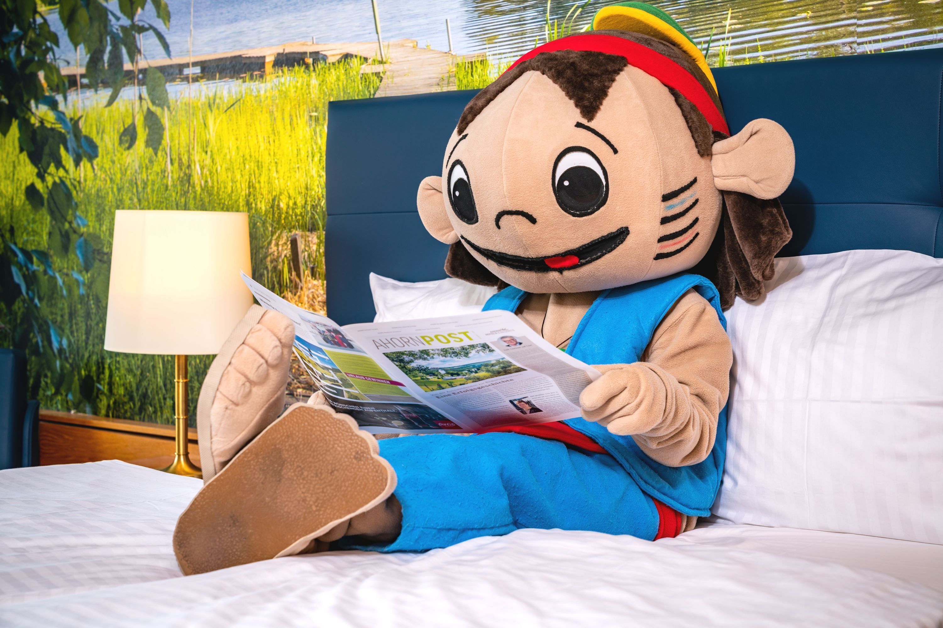 A plush toy character sitting on a bed, reading a magazine.
