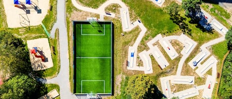 An aerial view of a sports complex with a tennis court, multiple sports fields, and parking areas.