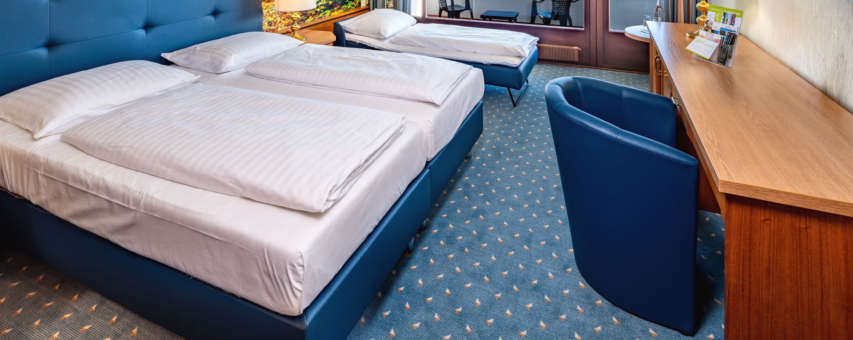 Ein Hotelzimmer mit zwei Betten, einem Schreibtisch, einem Stuhl und einem kleinen Tisch.