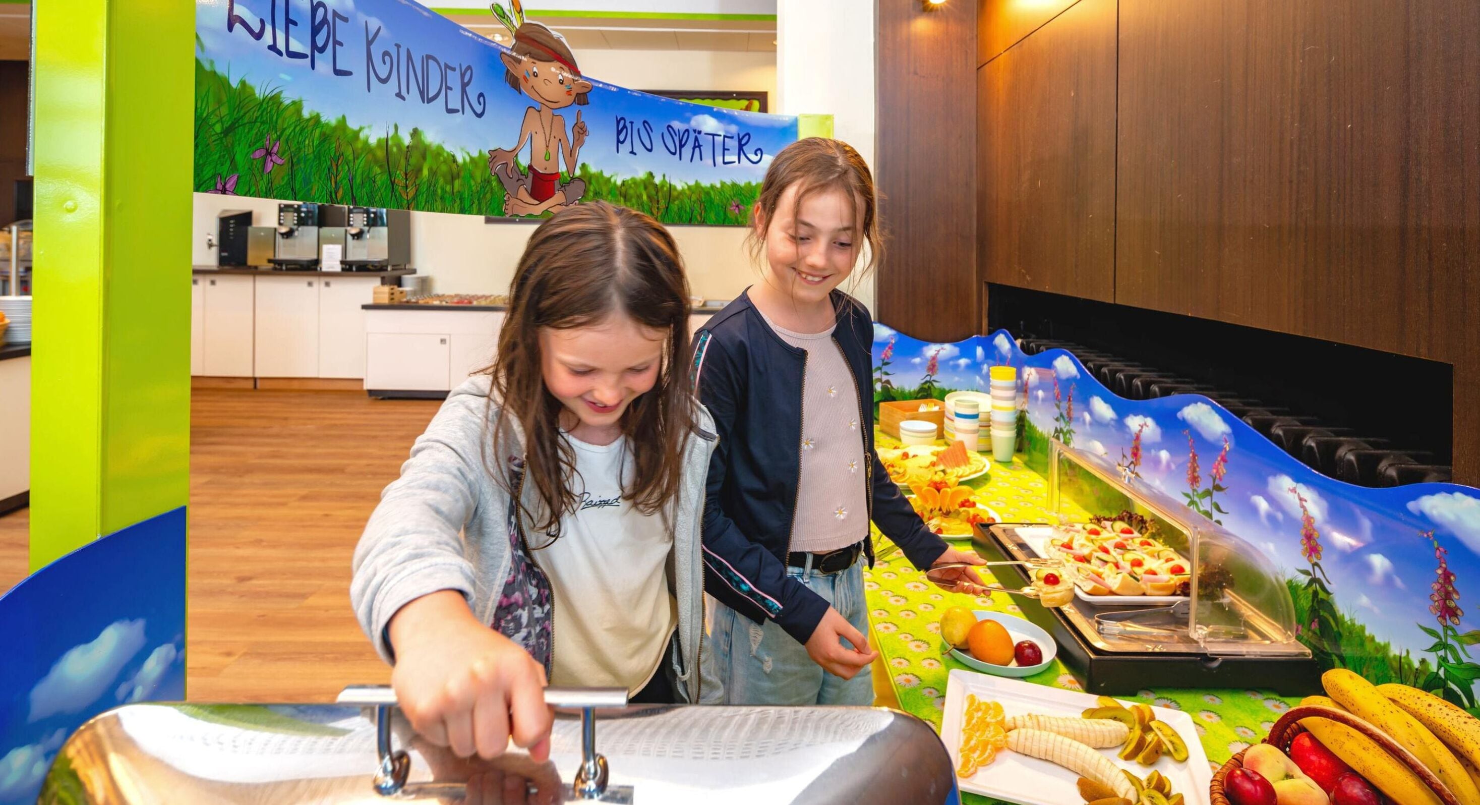 A kitchen area with a child and an adult, a buffet table with various food items, and a backdrop with a nature scene and text.