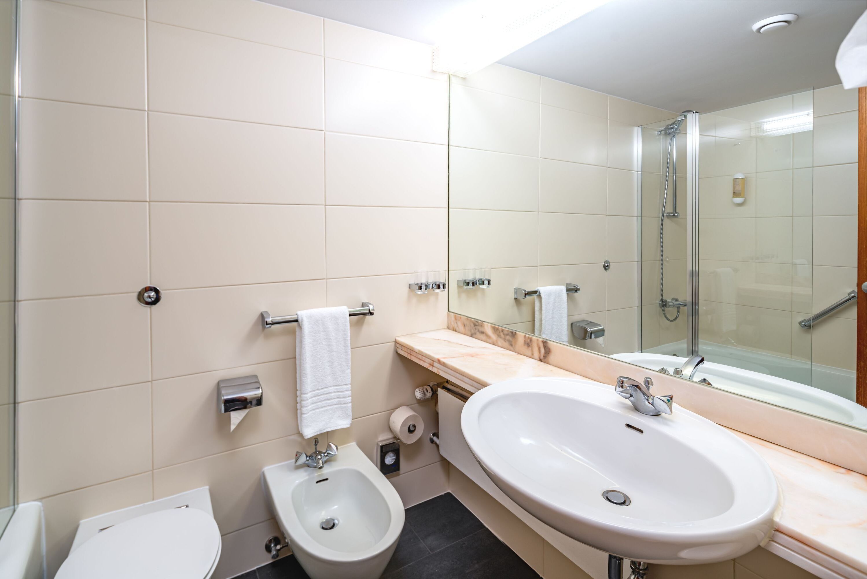A modern bathroom with a bidet, a sink, a toilet, and a glass-enclosed shower.
