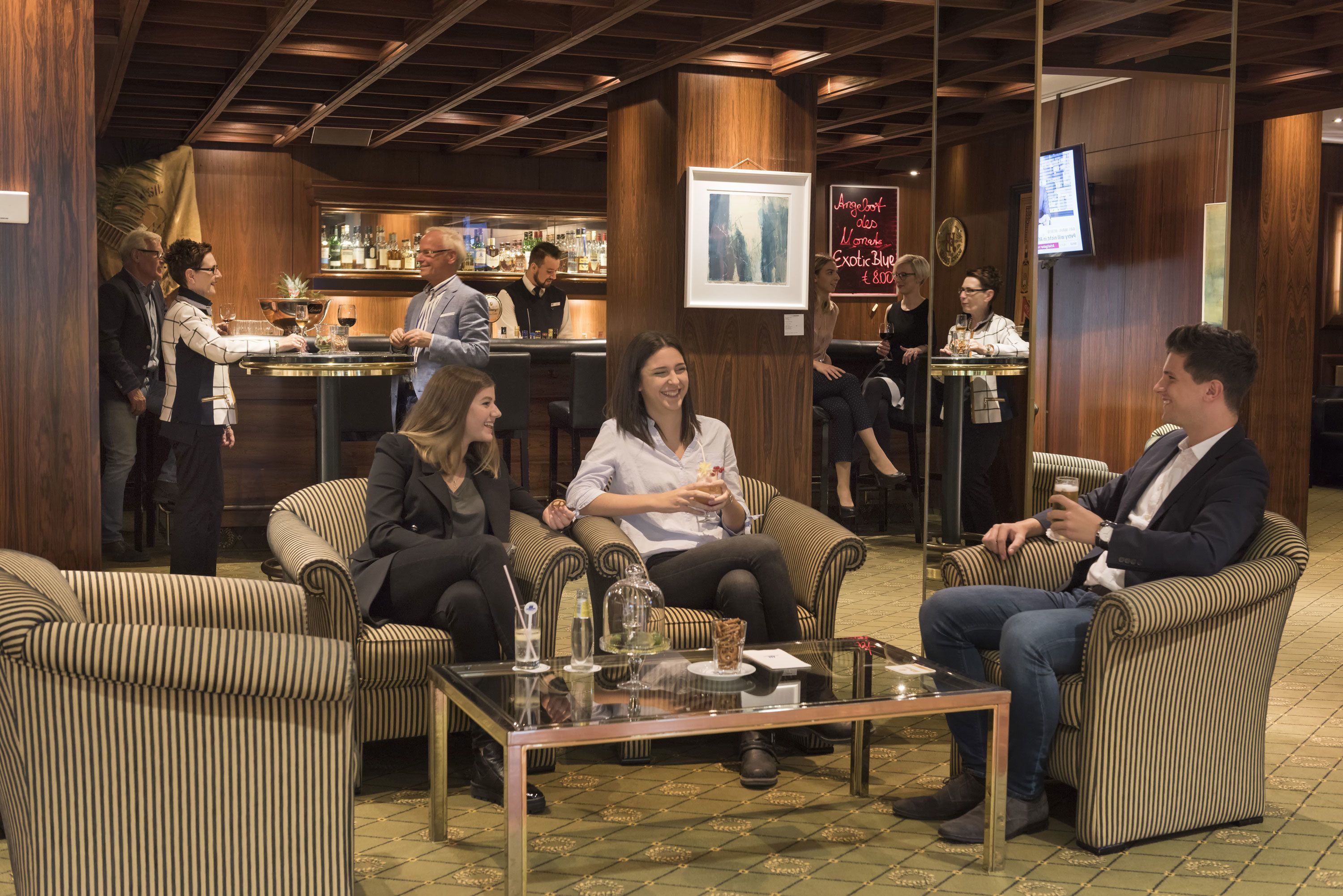 A bar area with striped upholstered chairs, a bar counter, and a television screen.