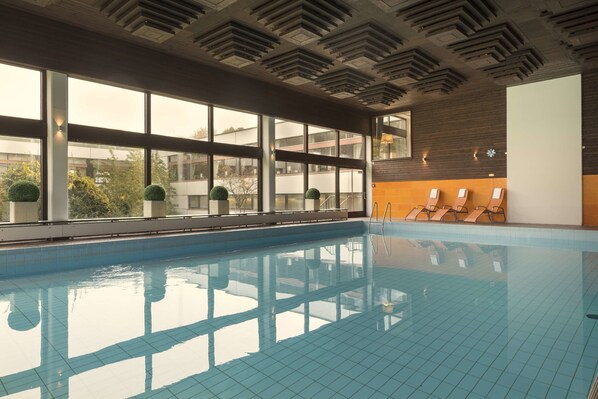 An indoor swimming pool with clear windows, a tiled floor, and sun loungers along the side. - Maritim Hotel Bellevue Kiel (Kiel)