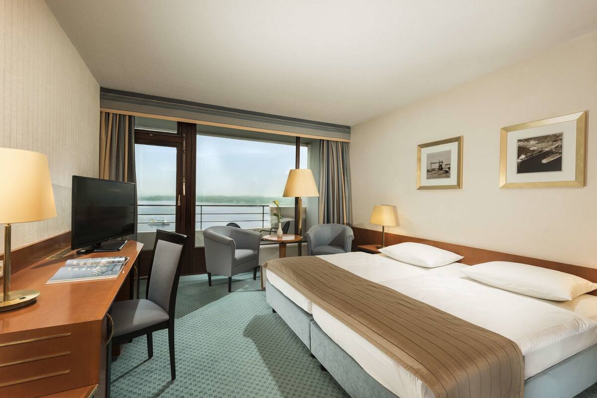 Ein Hotelzimmer mit Bett, Schreibtisch, Stühlen, Fernseher und einem Fenster mit Aussicht.