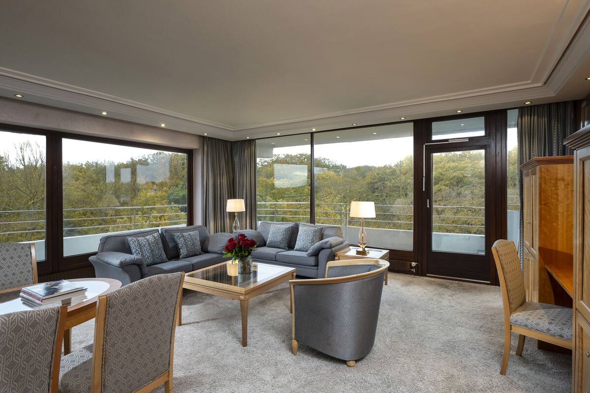 Ein modernes Hotelzimmer mit einer großen Couch, einem Couchtisch und Blick ins Freie durch große Fenster.