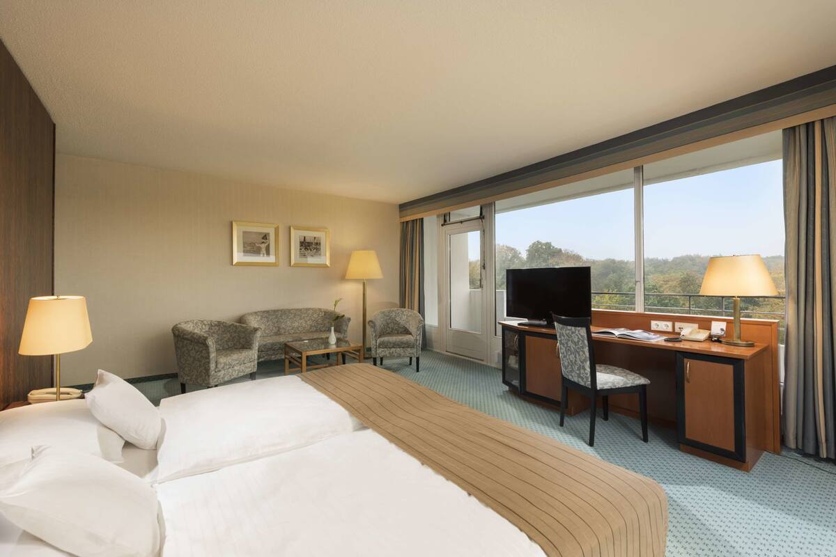 Ein Hotelzimmer mit einem großen Bett, einem Schreibtisch mit Stuhl, einem Fernseher und Blick ins Freie.