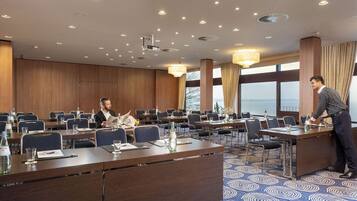 Un salón de conferencias con varias mesas, sillas y un amplio ventanal con vistas.