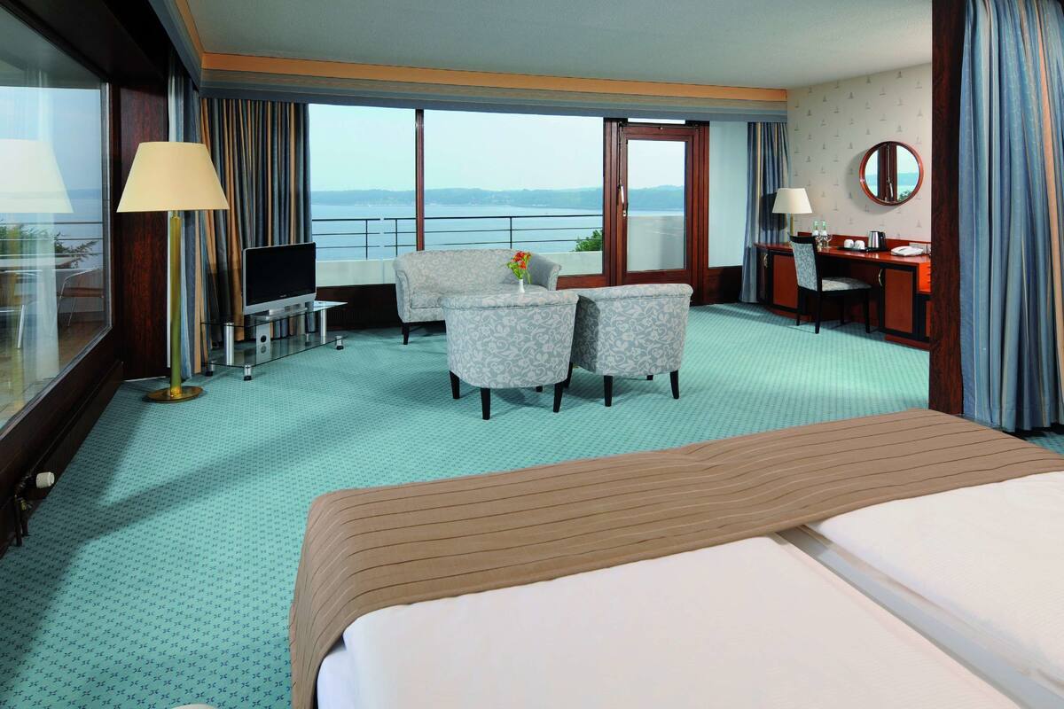 Ein Hotelzimmer mit einem großen Bett, einem Schreibtisch mit Stuhl, einem Fernseher und Blick auf das Meer.