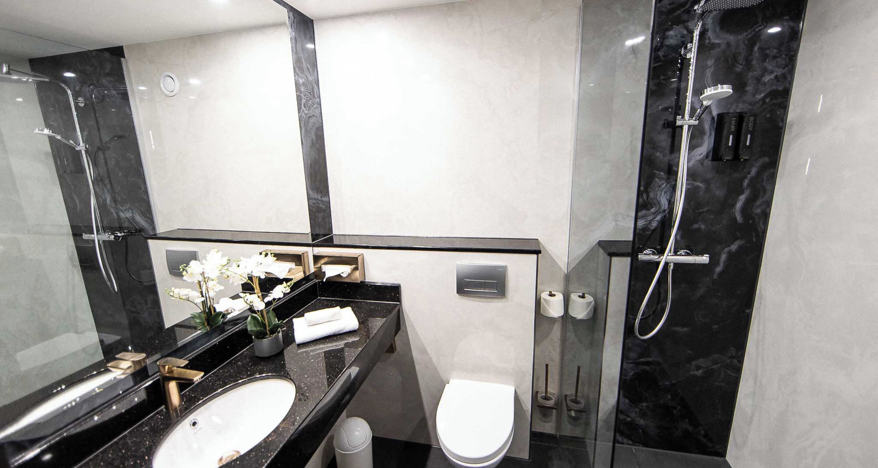 Un baño moderno con tocador de mármol negro, inodoro blanco y cabina de ducha con mampara de vidrio.