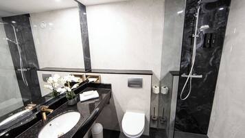 Un baño moderno con tocador de mármol negro, inodoro blanco y cabina de ducha con mampara de vidrio.