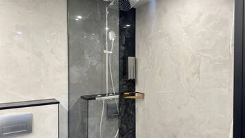 A modern shower enclosure with a glass door, a handheld showerhead, and a black marble wall.