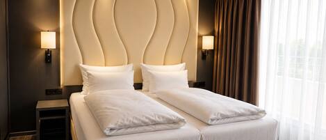 Habitación de hotel con una cama grande, dos lámparas de noche, cabecera con diseño único y una ventana con cortinas.