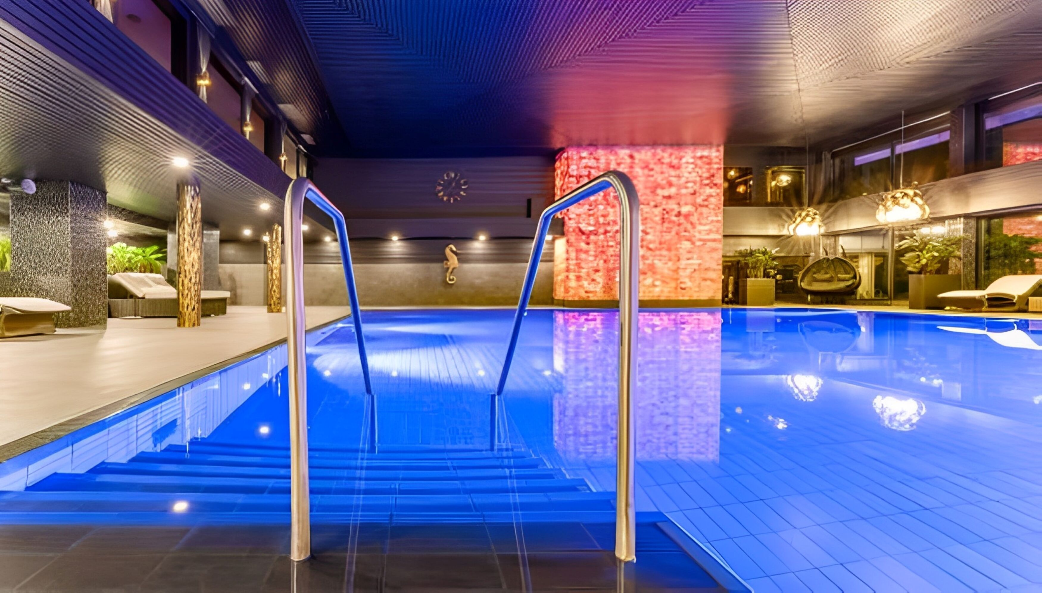 An indoor swimming pool with blue lighting, a seahorse decoration, and a staircase leading into the pool.