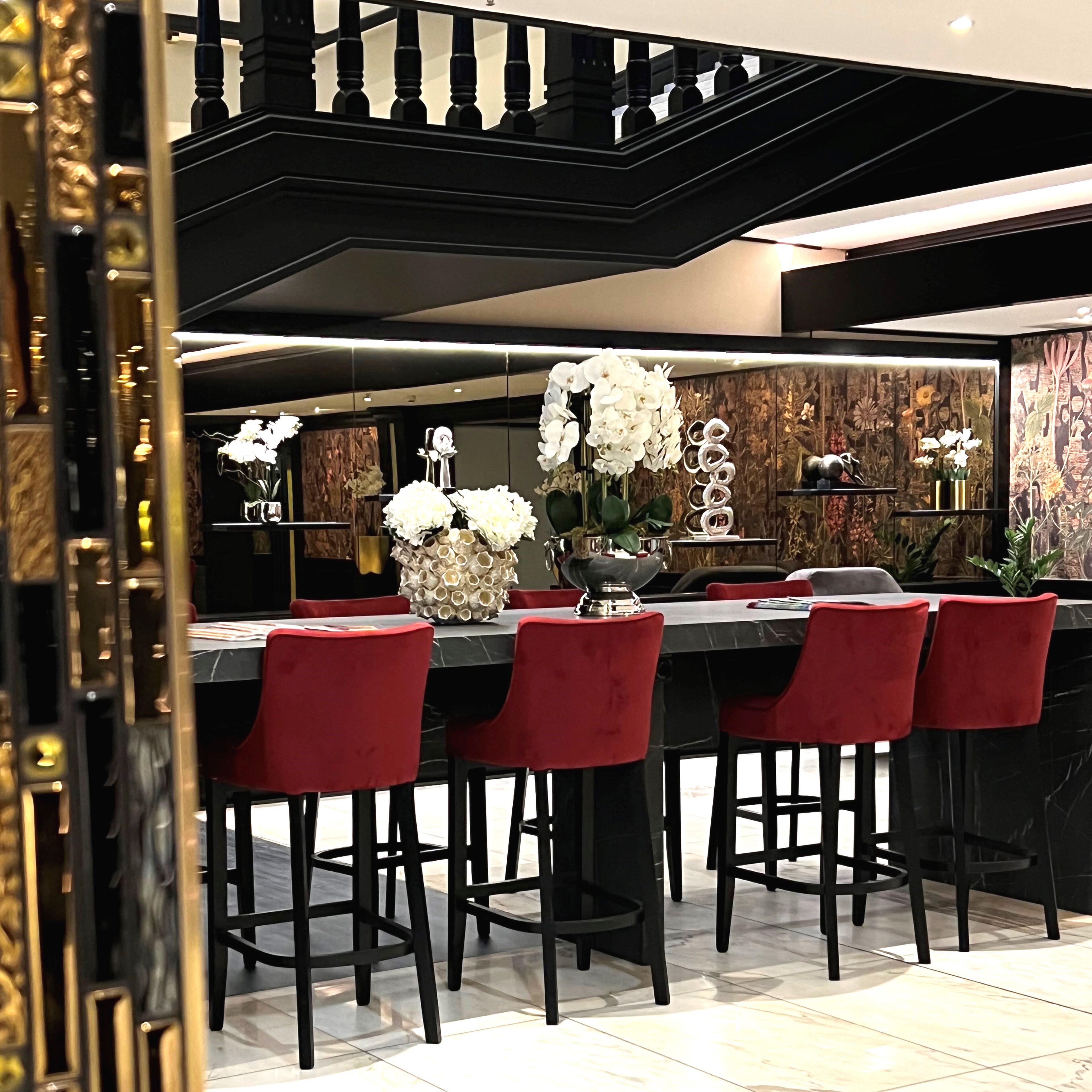 A modern bar area with a black countertop, red bar stools, and white floral arrangements.