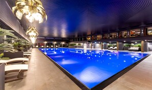 A large indoor swimming pool with a modern design, surrounded by lounge areas and a ceiling with a unique pattern. - PLAZA Premium Timmendorfer Strand (Timmendorfer Strand)