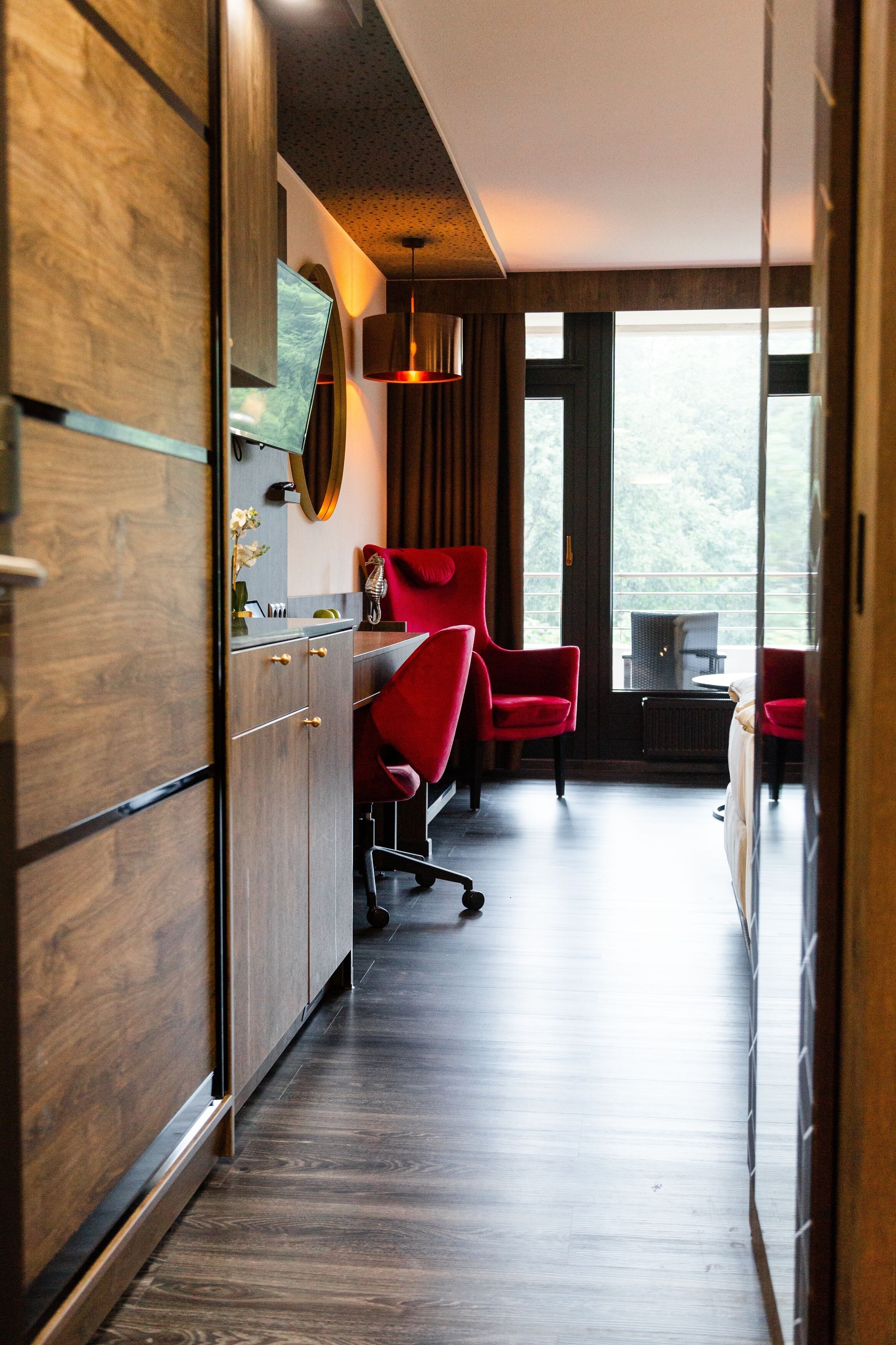 Un intérieur moderne avec des meubles en bois, des chaises rouges et une vue dégagée sur l’extérieur grâce à une grande fenêtre.