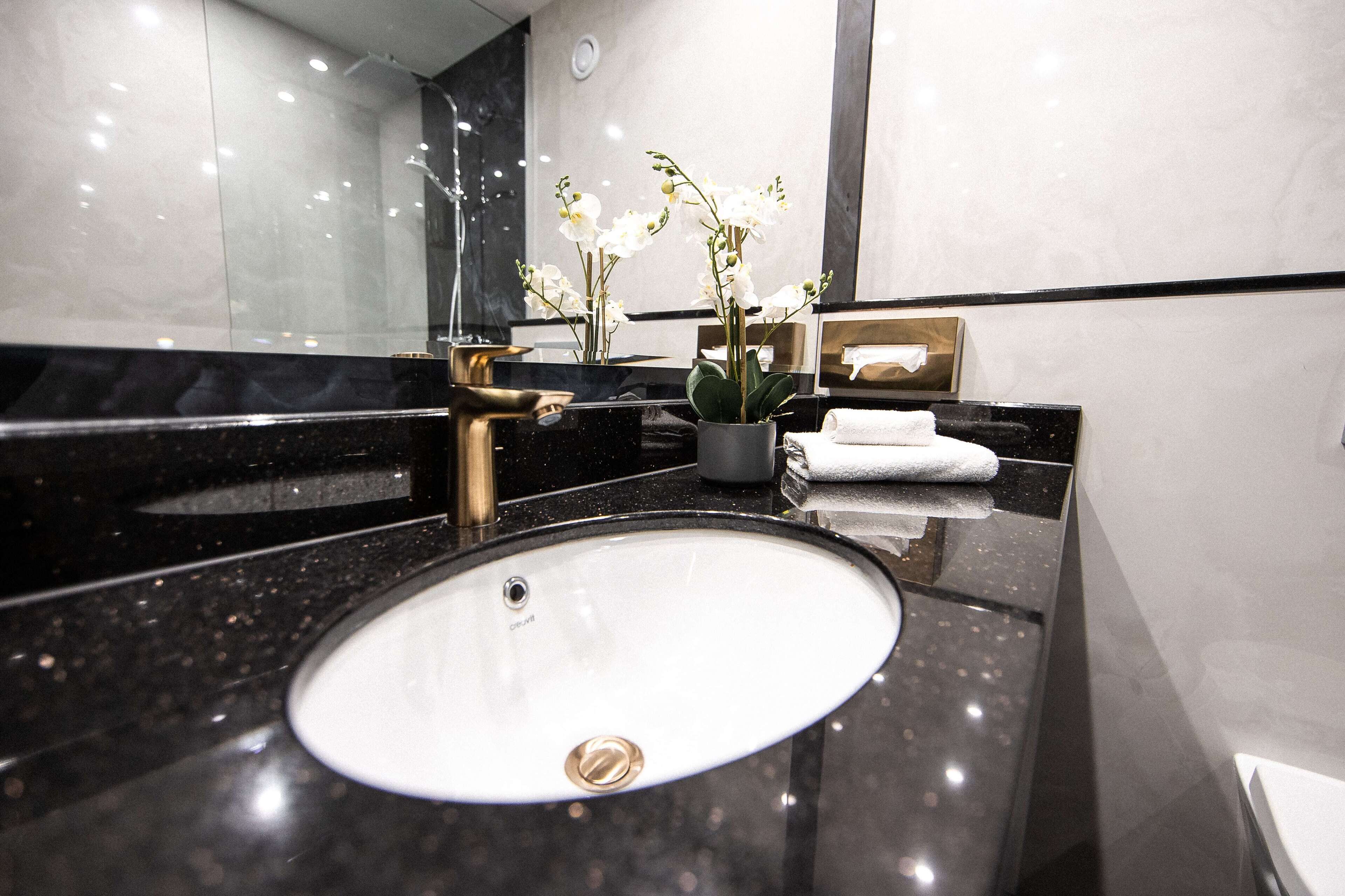 Ein modernes Badezimmer mit einer schwarzen Granittafel, einem weißen Waschbecken und einem großen Spiegel.