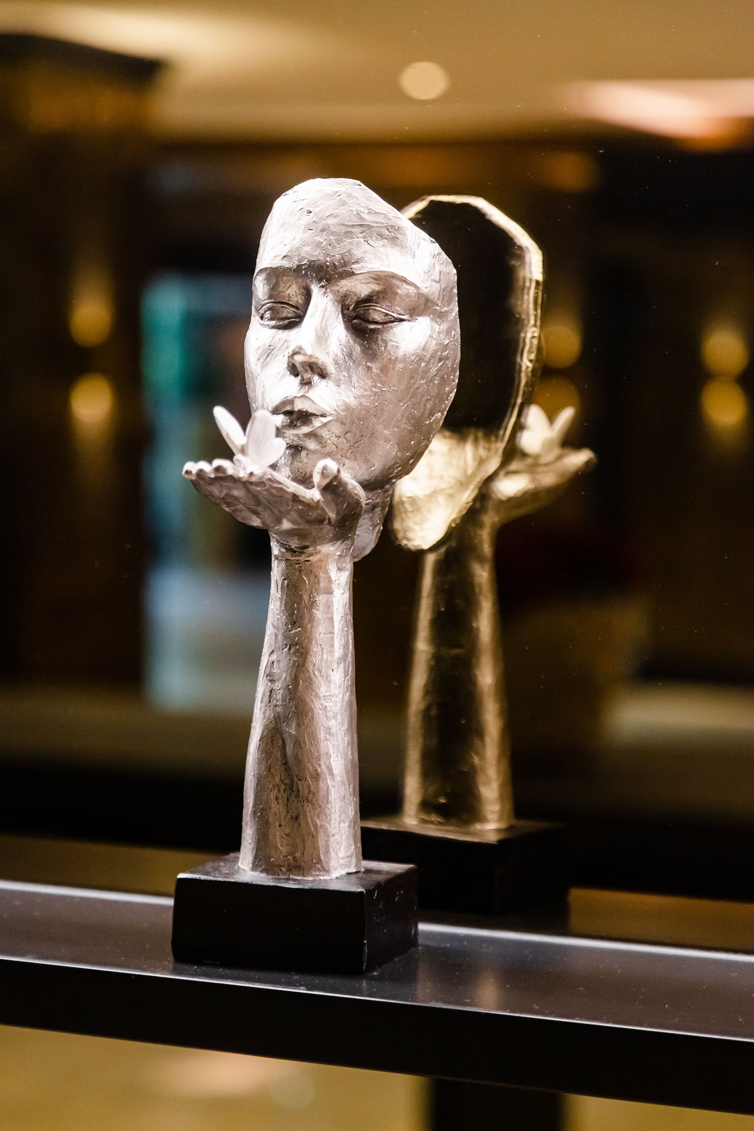 A sculpture of a face with a hand extended, displayed on a black pedestal.