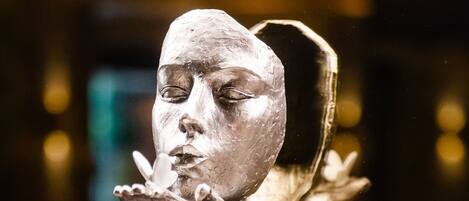 A sculpture of a face with a hand extended, displayed on a black pedestal.