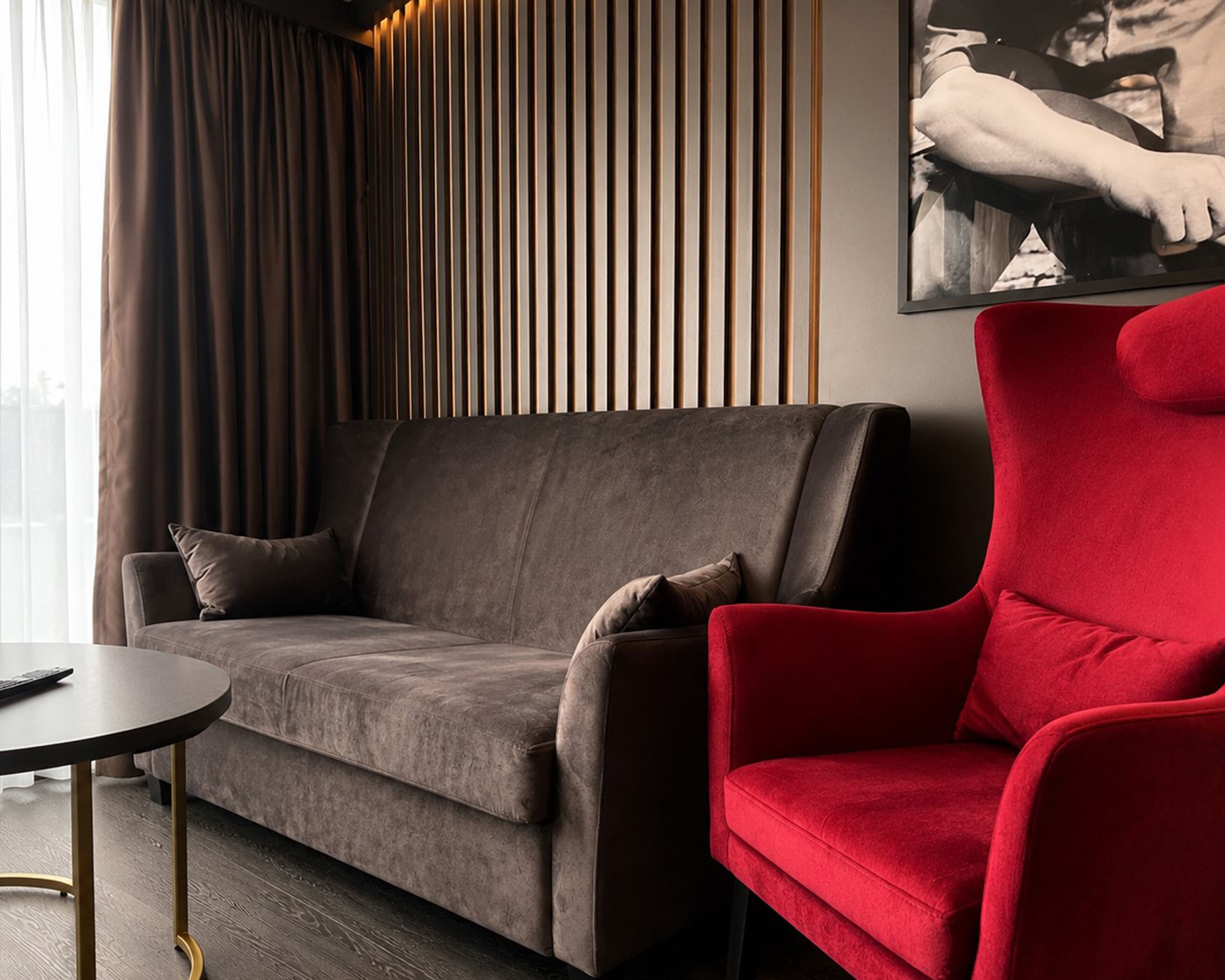 Een moderne woonkamer met een grijze bank, een rode fauteuil, een klein rond tafeltje en een verticale houten wandpaneel.