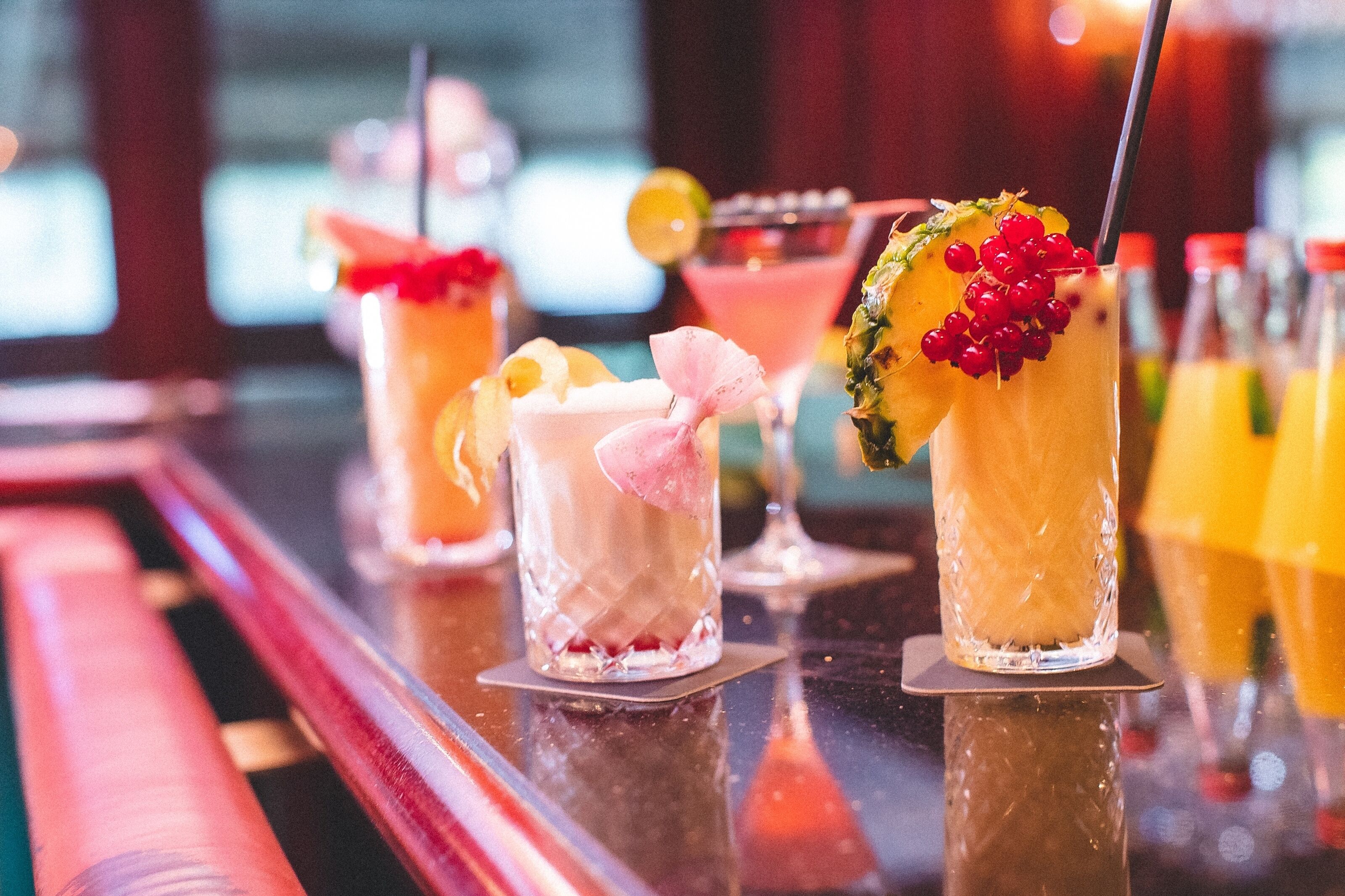 Un bar con varios cócteles, incluyendo una bebida de piña con bayas rojas y una bebida rosa con un lazo.