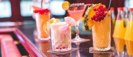 A bar with various cocktails, including a pineapple drink with red berries and a pink drink with a bow.