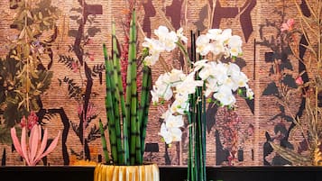 Two tall, yellow, ribbed vases with white orchids on a tiled floor against a patterned wall.