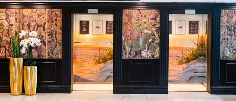 A lobby with a reception desk, two large potted plants, and a mural depicting a beach scene.