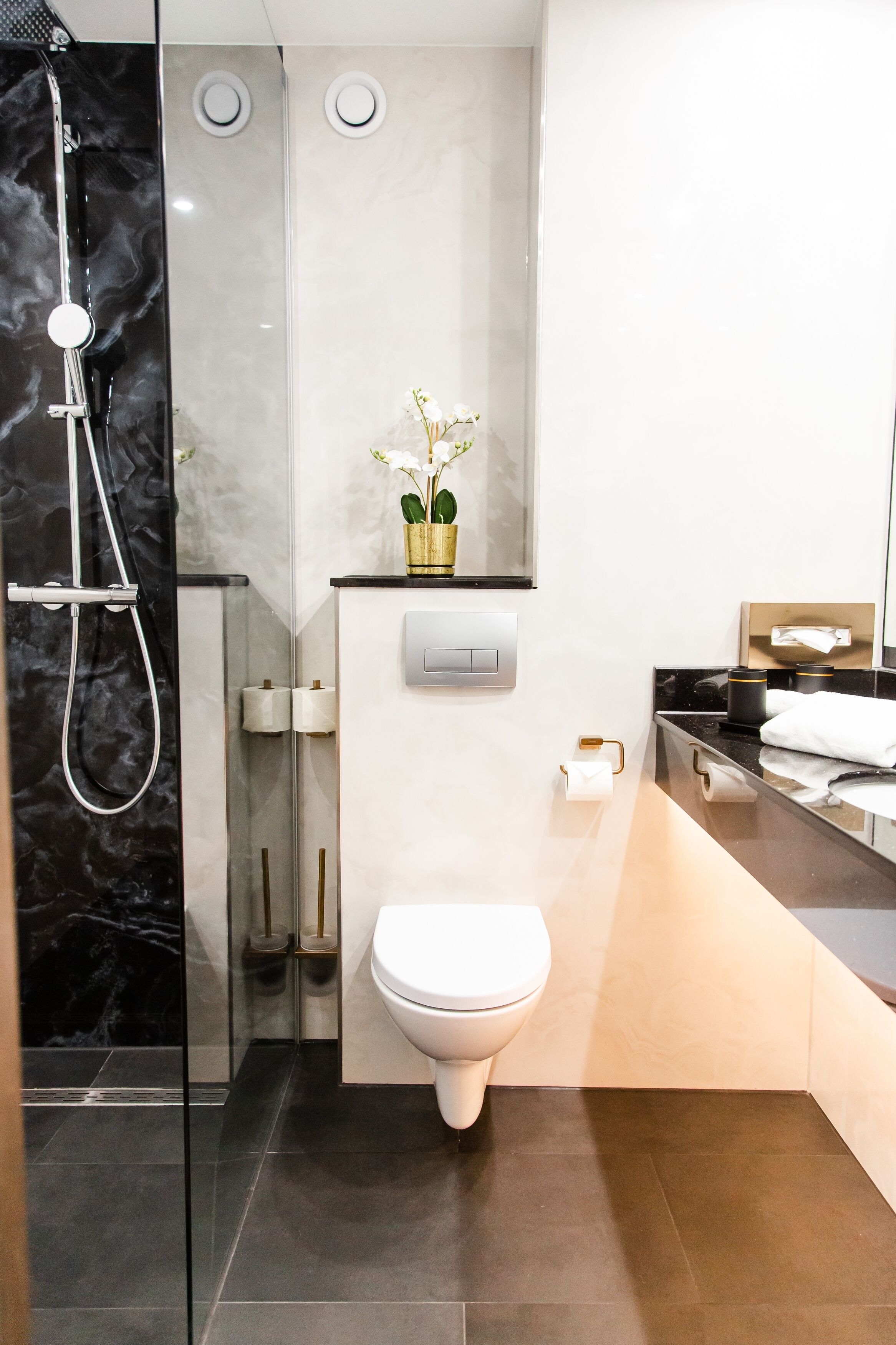 A modern bathroom with a glass-enclosed shower, a toilet, and a sink area.