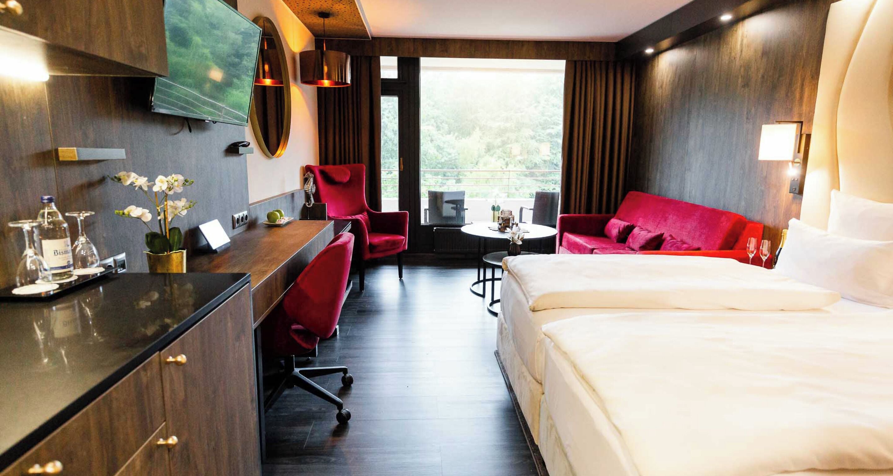Une chambre d’hôtel avec un lit, un bureau, un canapé rouge et une table à manger.