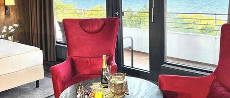 A room with a red chair, a table with a bottle, a glass, and a fruit plate.