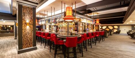 A bar area with red bar stools, a central bar counter, and overhead pendant lighting.