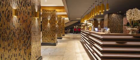 A modern lobby with a marble floor, a reception desk, and a staircase.