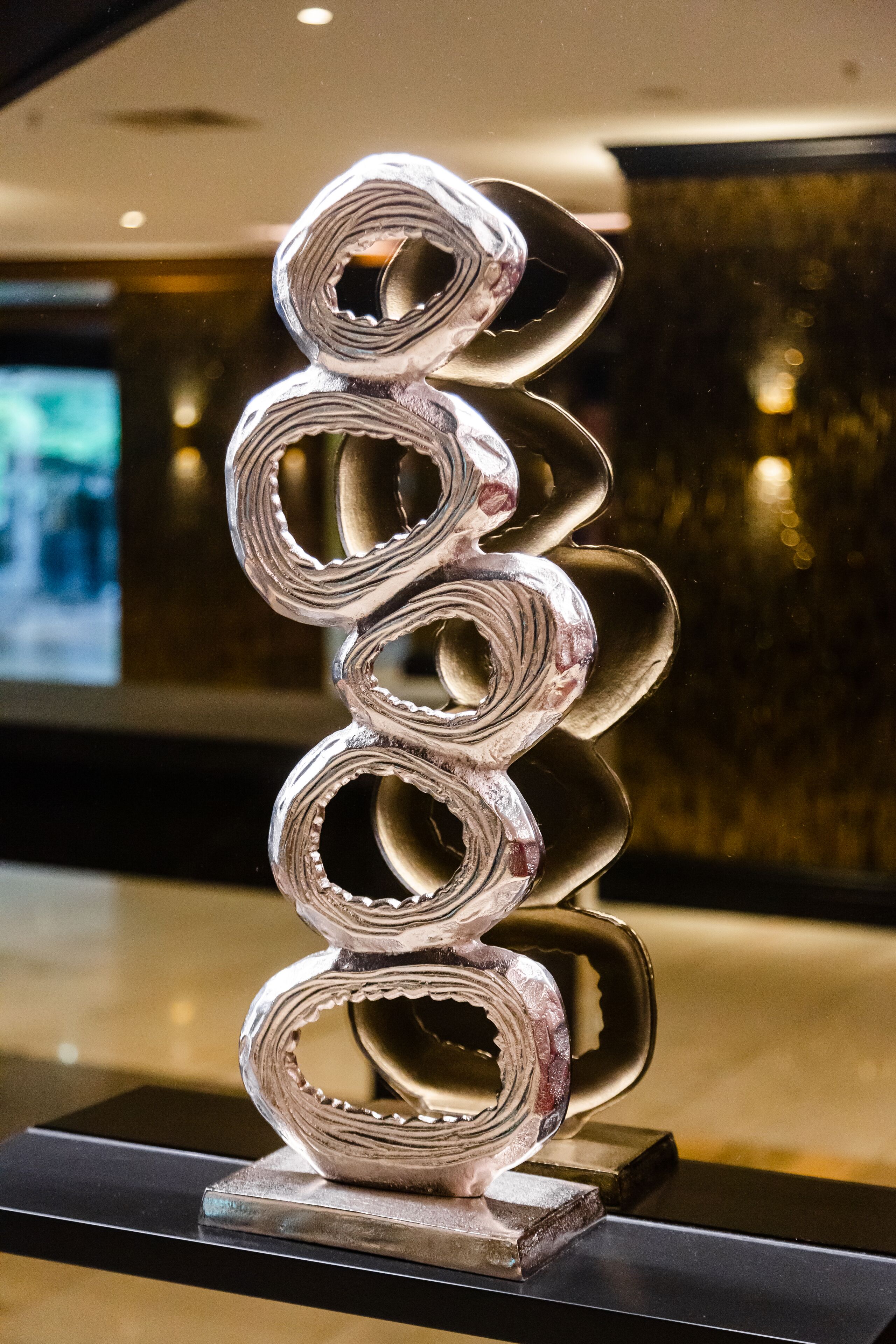 A metallic sculpture with a spiral design, displayed on a black pedestal in a well-lit indoor space.
