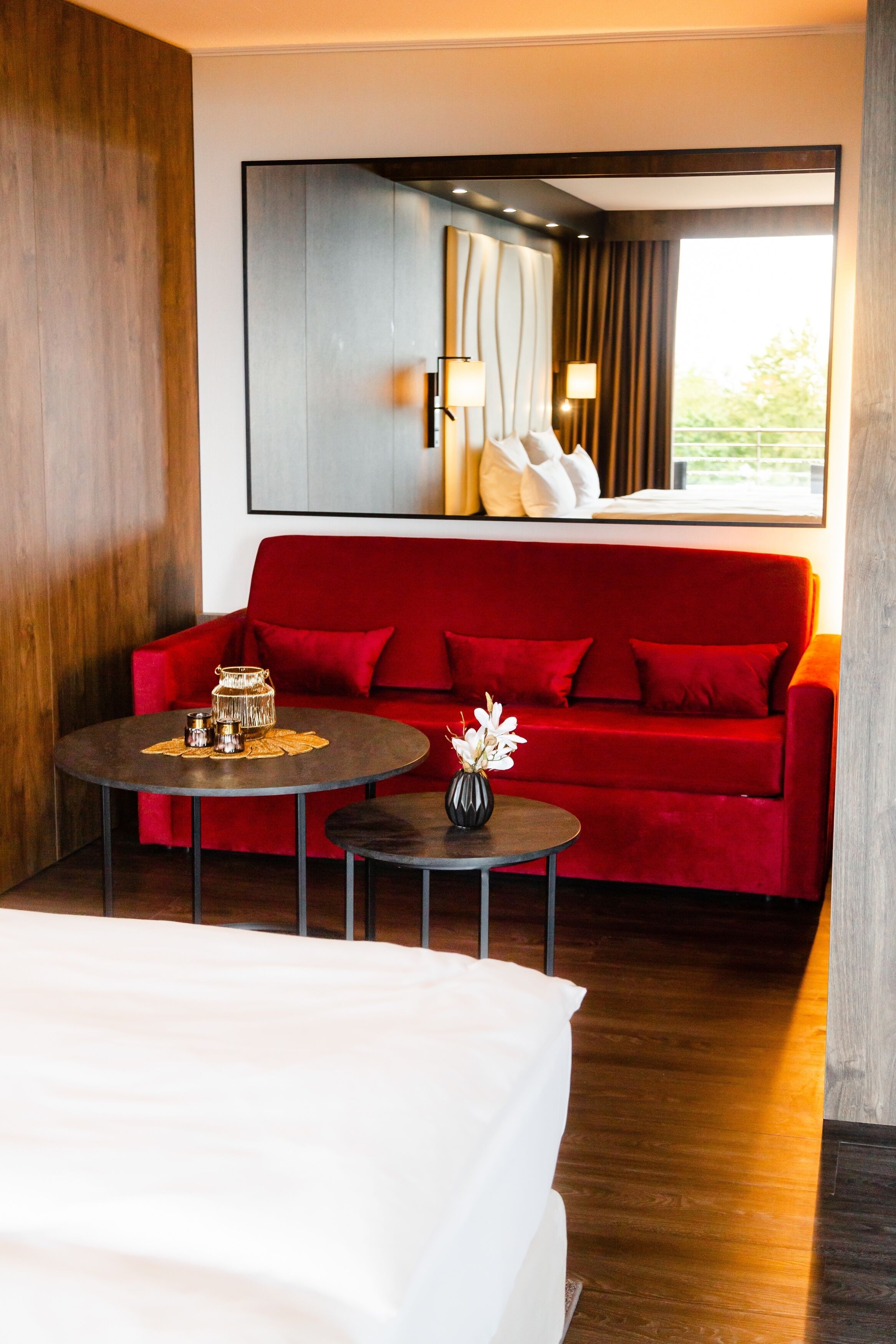 A hotel room with a red sofa, a round coffee table, a small side table, and a bed.