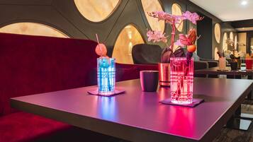 A modern bar area with two illuminated glasses on a table, a red sofa, and a decorative wall with circular patterns.
